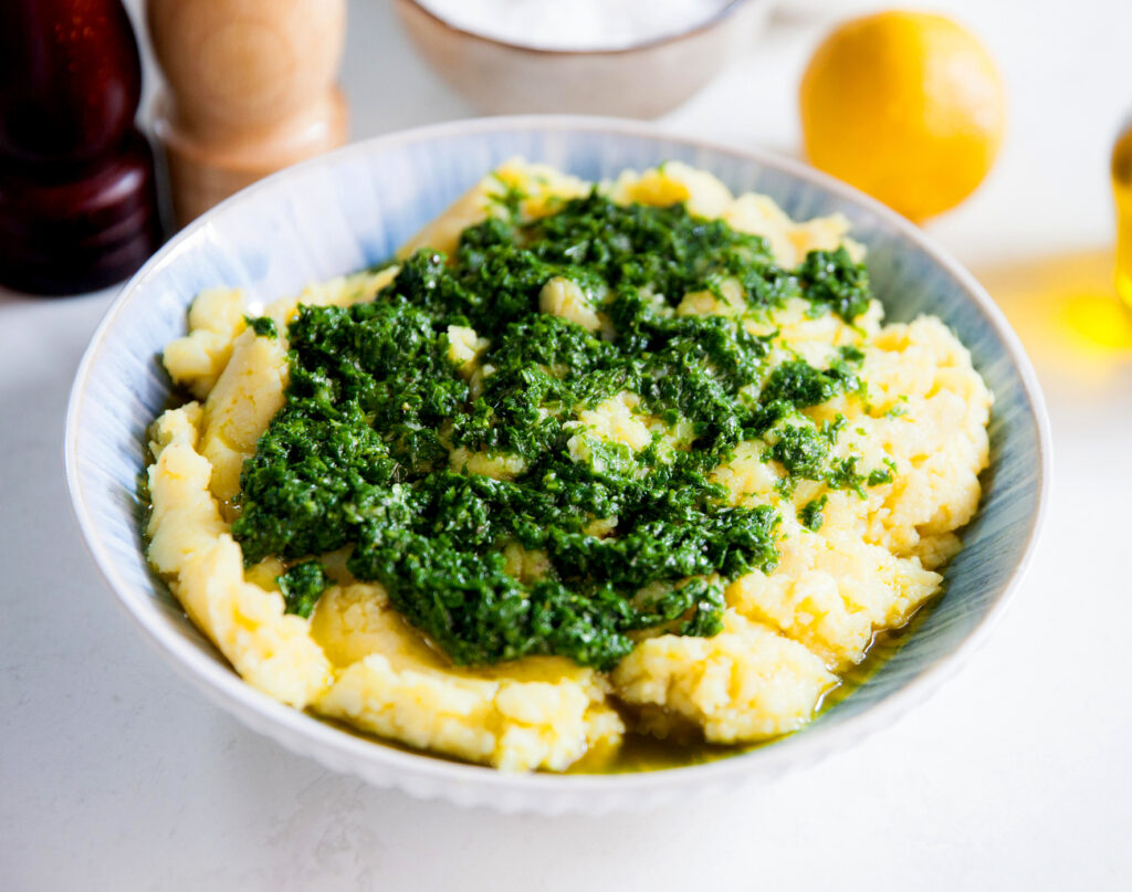 Image of mashed potato in a bowl topped with a green herb sauce.