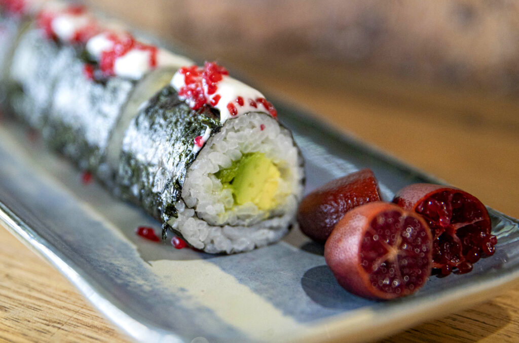 A neatly cut roll of sushi served on a tray with a side of finger lime.