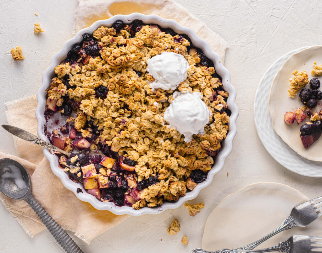 Overhead shot of a dessert crumble in a pie dish, topped with scoops of ice cream.