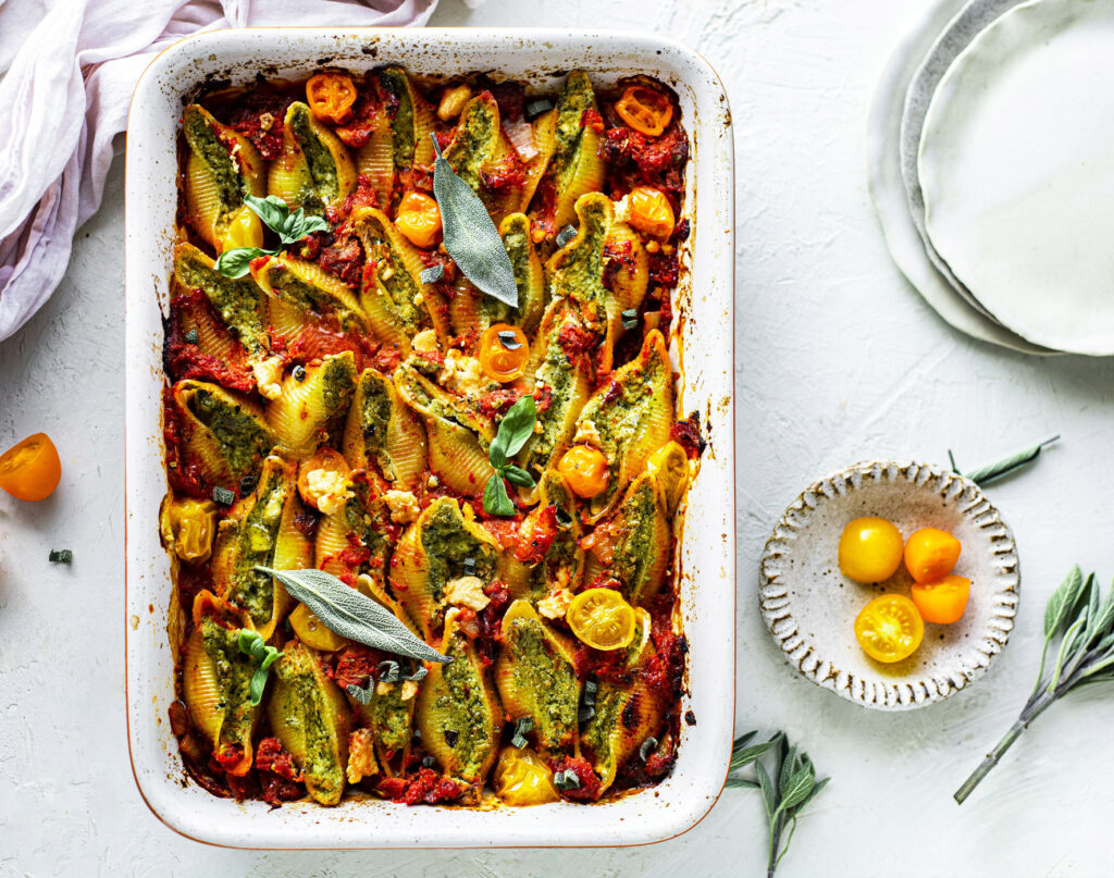 A rectangular baking tray filled with tomato sauce and spinach and ricotta filled past shells. A side dish of cherry tomatoes sits off to the side.