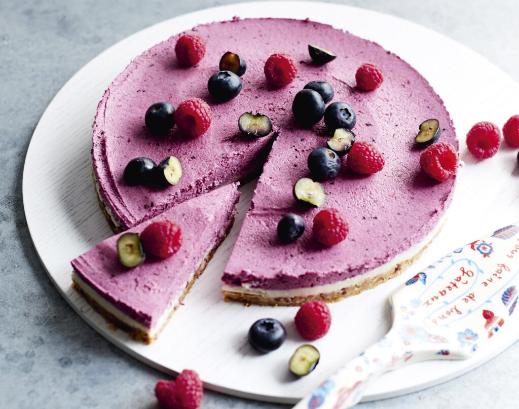 An image of a bright purple cheesecake topped with colourful fruit.