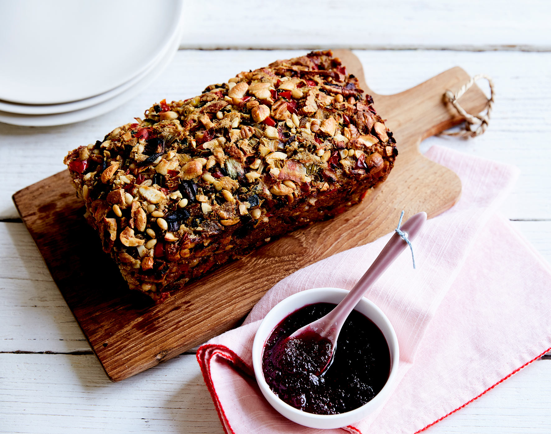 A rectangular nutloaf sits on a wooden serving board, with a side of cranberry sauce.