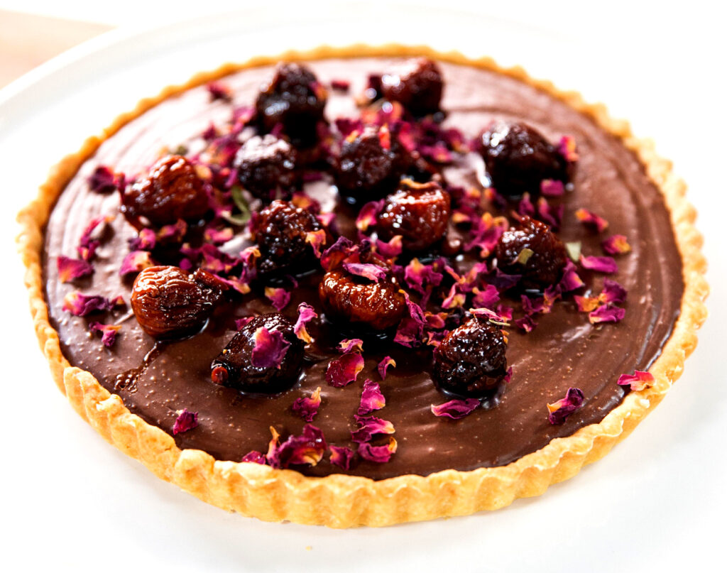 A close up from above of a full chocolate tart topped with spiced figs and dried rose petals.