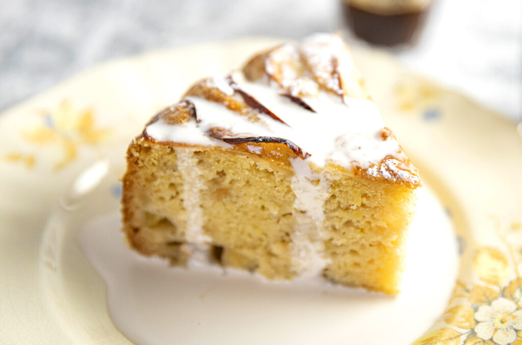 A close-up image of a slice of teacake on a plate drizzled with cream.