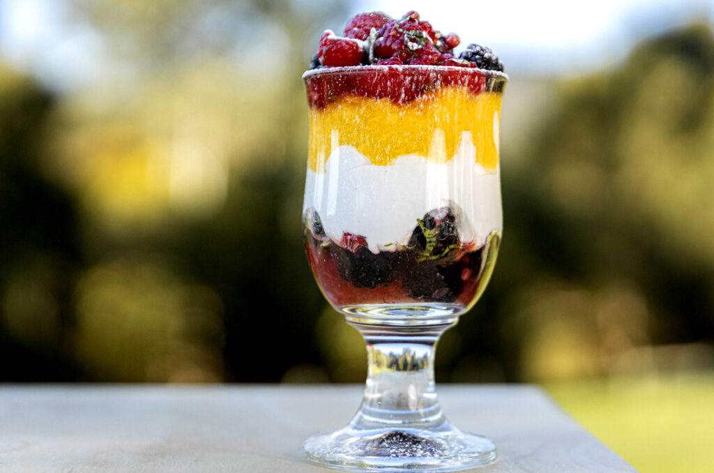 An individual serving of trifle in a clear glass on an outdoor table. 