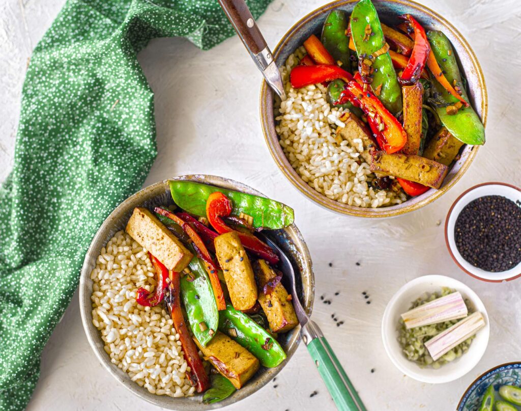 Overhead shot of two bowls of tofu and veggie stir-fry served with brown rice.