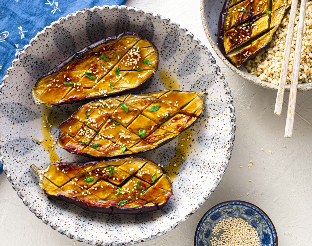 Three eggplant halves sit in a bowl covered in a miso glaze.