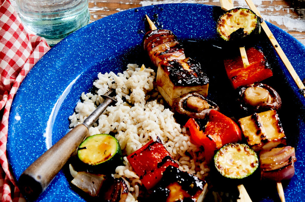 A plate of teriyaki tofu skewers, with capsicum, zucchini, mushroooms and rice.