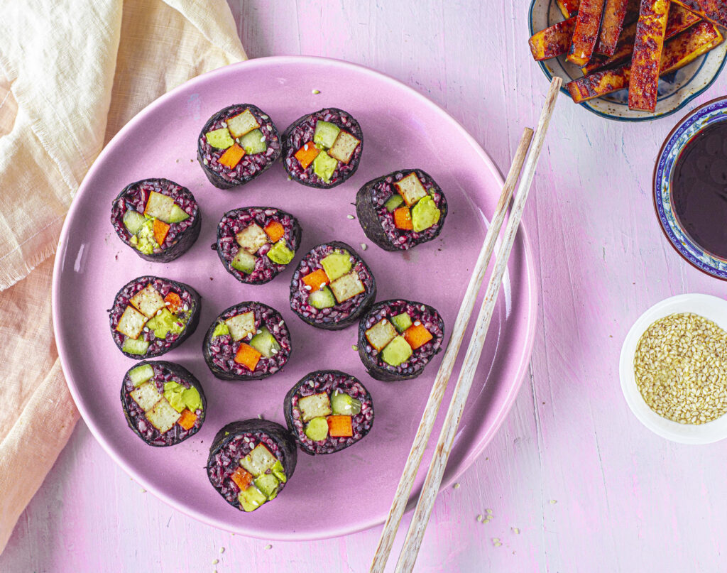 A purple plate featuring sushi made with black rice.