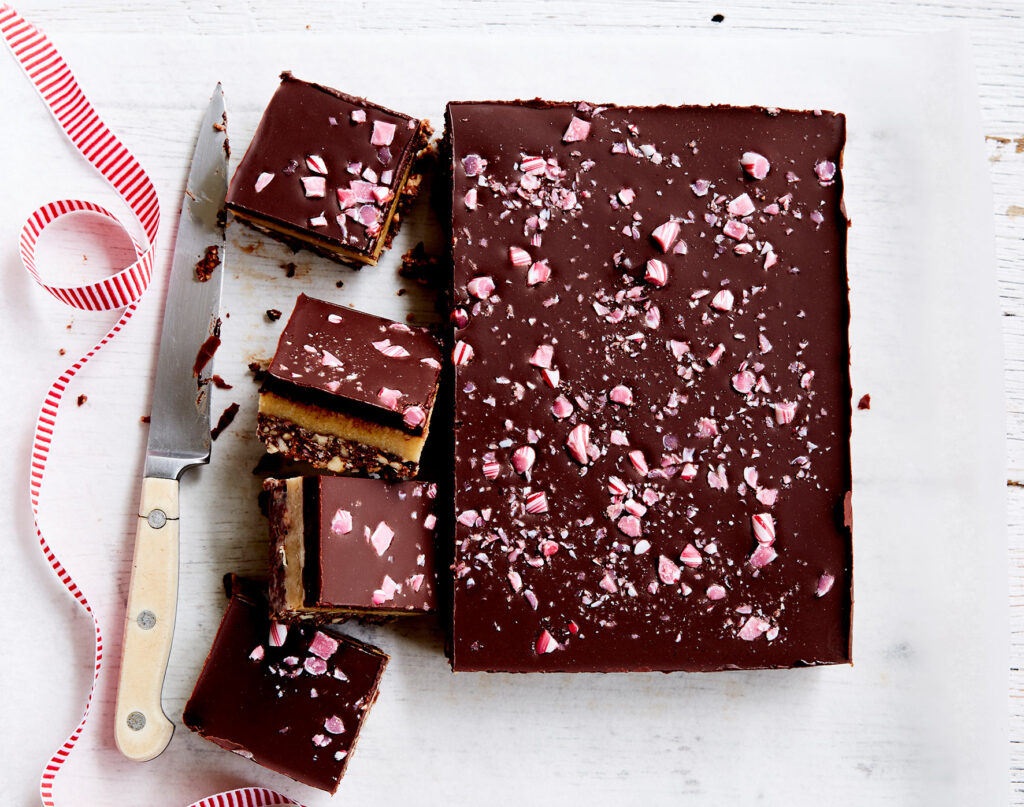 An overhead shot of a slab of peppermint fudge slice with four squares cut with a knife lying to the side.