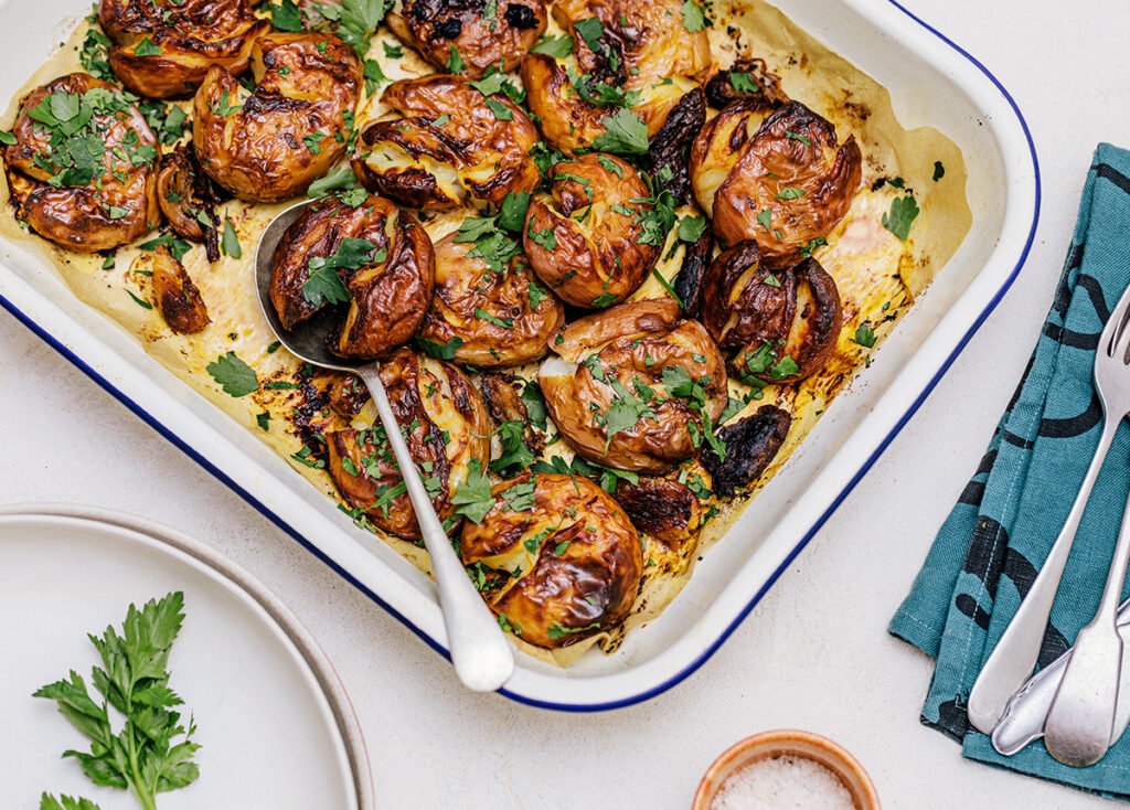 A rectangular oven tray sits on a table filled with crispy garlic roasted potatoes.