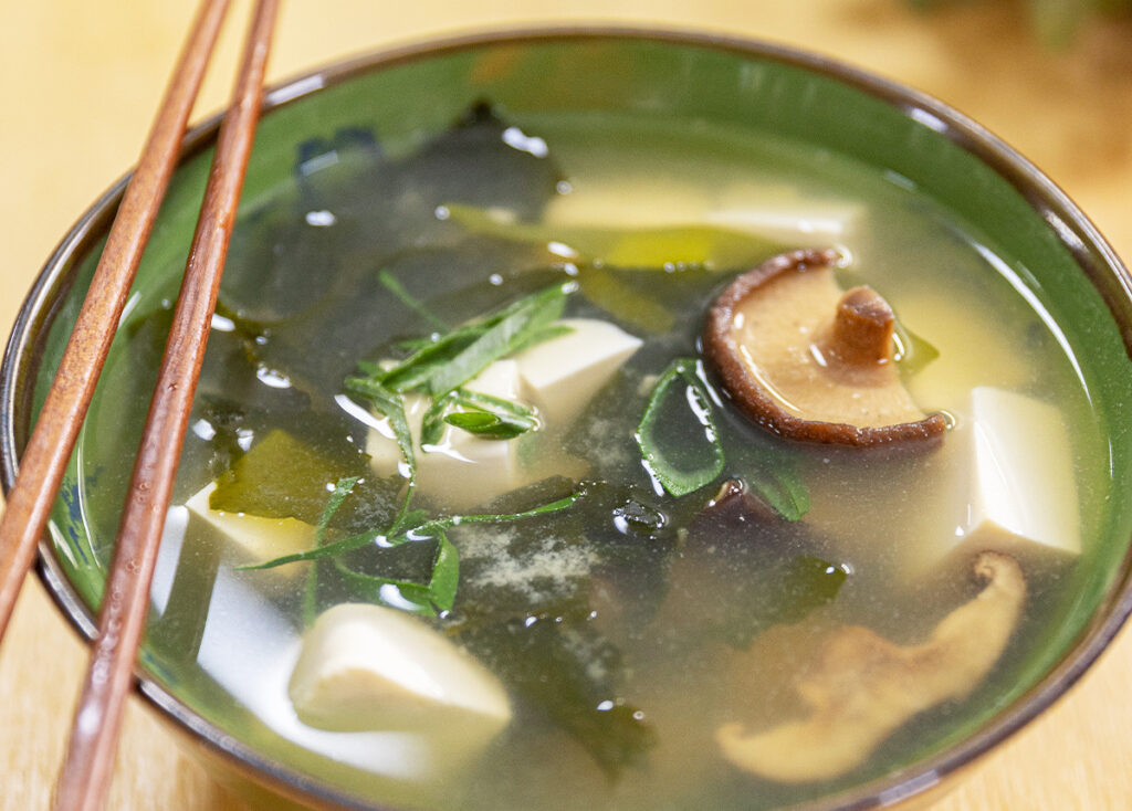 Mushroom, tofu, and greens in a bowl with clear broth.