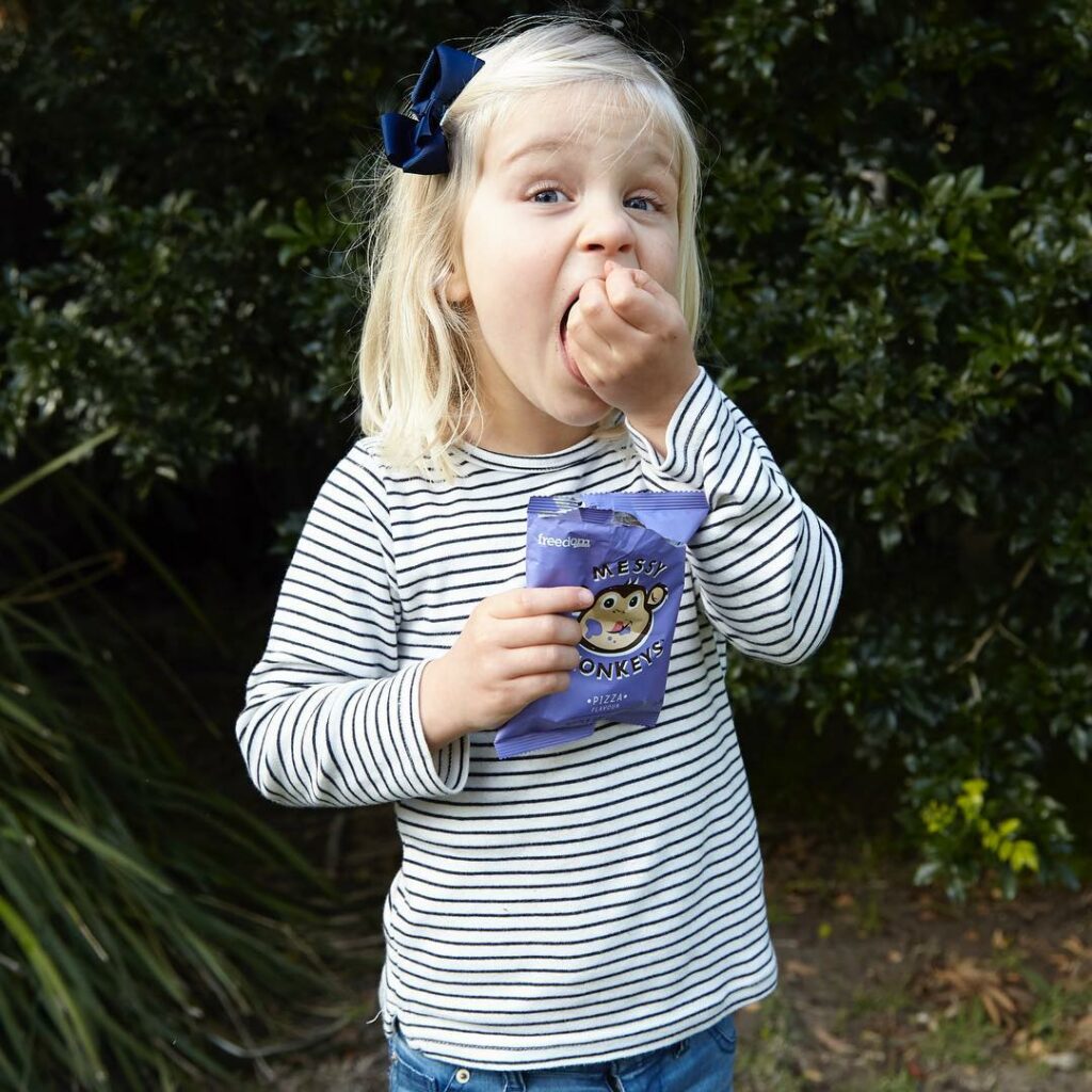 A young girl eating from a snack pack of Messy Monkeys savoury snacks.
