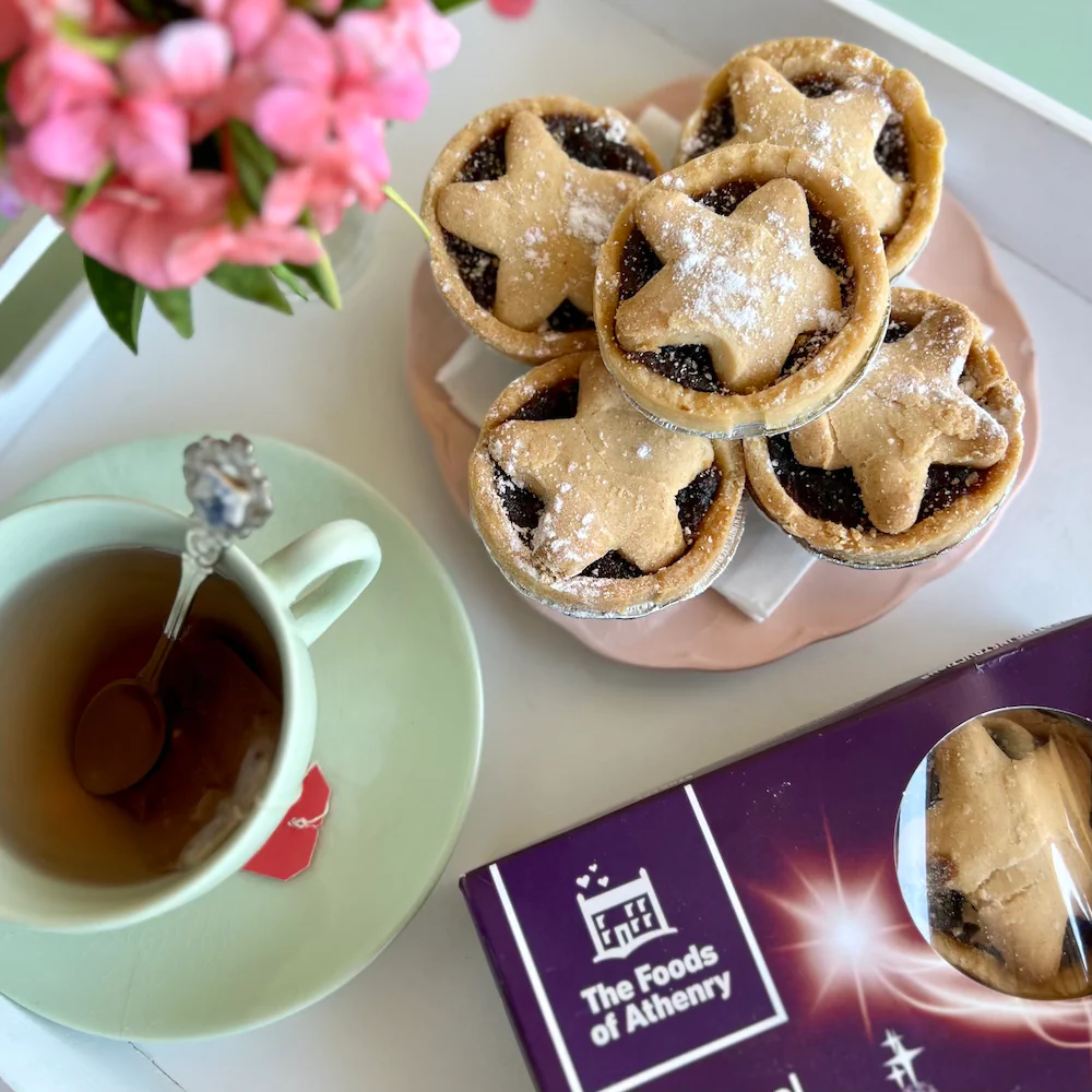 An overhead image with mince pies piled on a saucer next to a cup of tea.