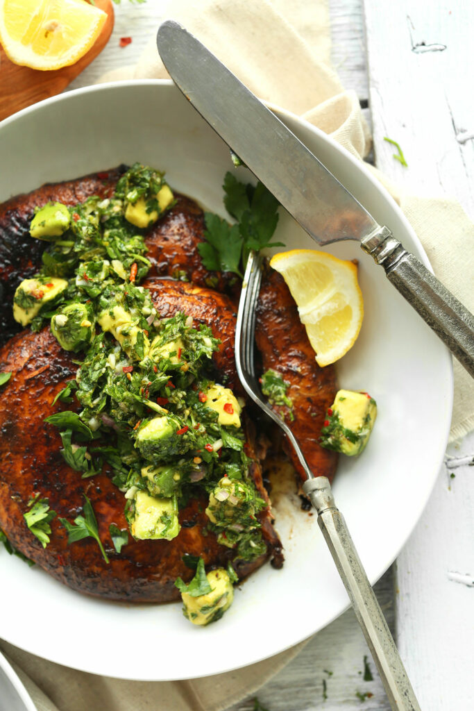 A bowl of grilled portobello steaks topped with chimichurri and served with a slice of lemon.