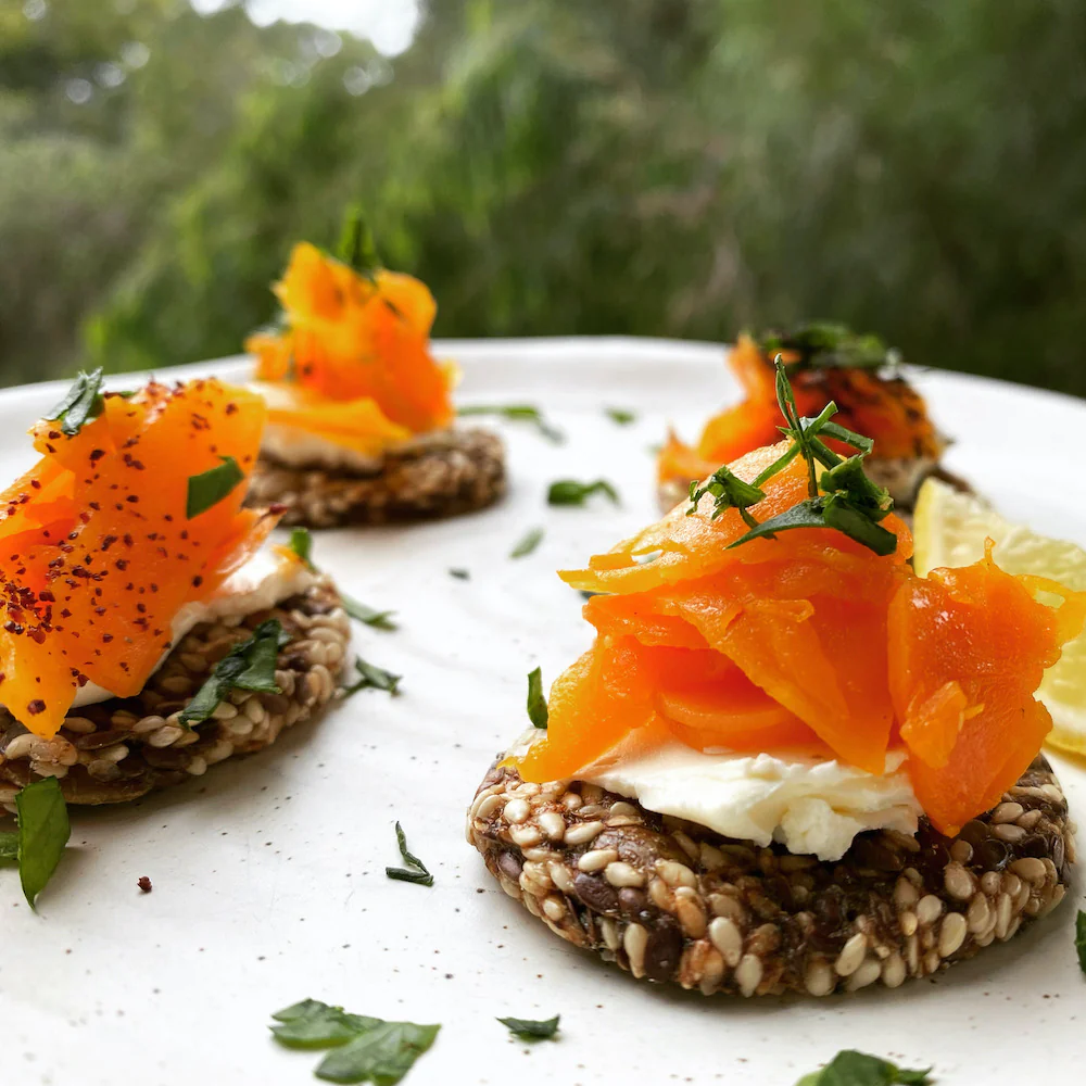 A serving platter with three servings of salmon and cream cheese on a grain fritter,