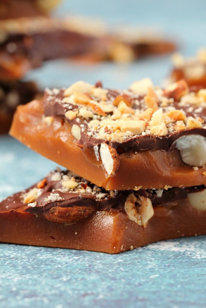 A close up of creamy toffee topped with chocolate and crushed nuts.