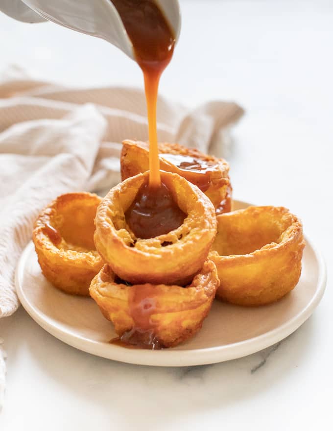 A plate piled high with Yorkshire puddings with gravy being poured from high above.