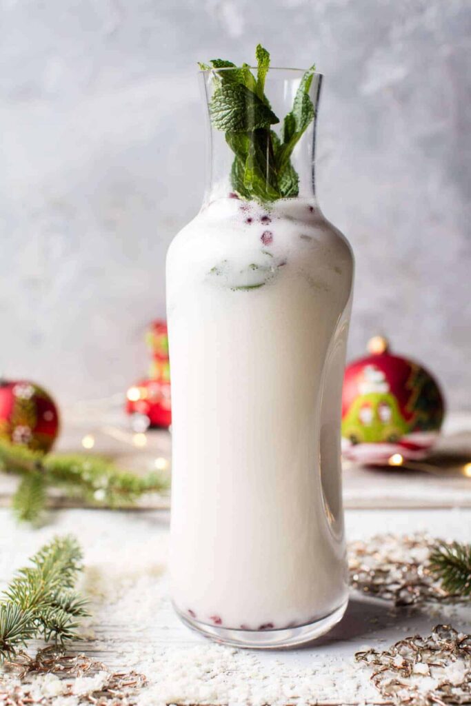 A tall glass jar of White Christmas Mojito on a table with Christmas decorations surrounding it.