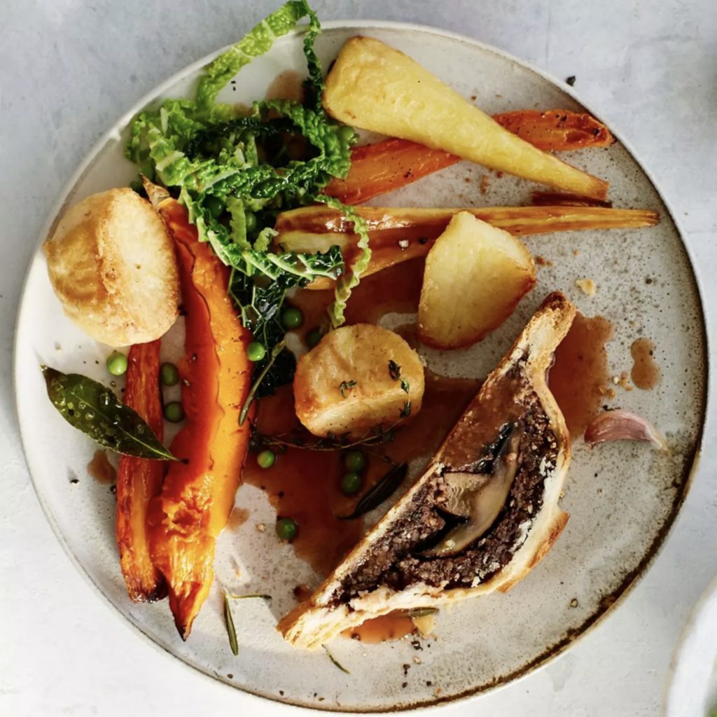 Image from above of a plate with a serve of mushroom wellington and a side of roast potato, parnsip and carrot. with gravy