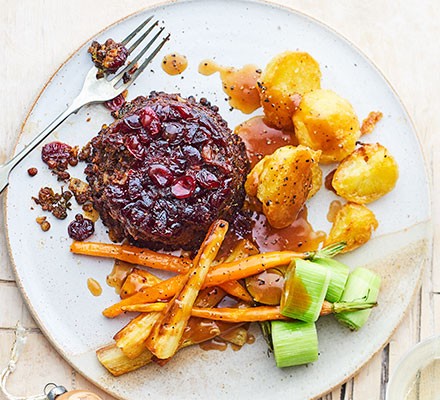 An overhead shot of a round lentil bake on a plate, smothered in cranberry sauce with a side of roast veg.