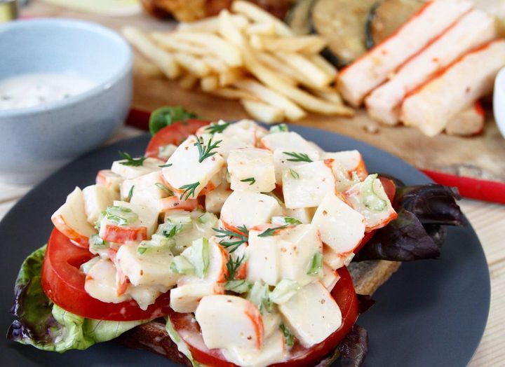 An open sandwich on a black plate, piled high with vegan crab meat smothered in egg-free mayo and dill.