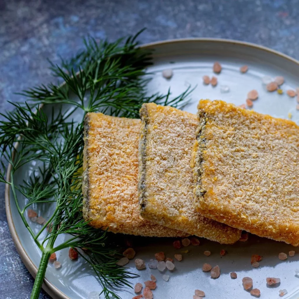 Crumbed fillets of plant-based fish on a plate with a sprig of herbs to garnish.