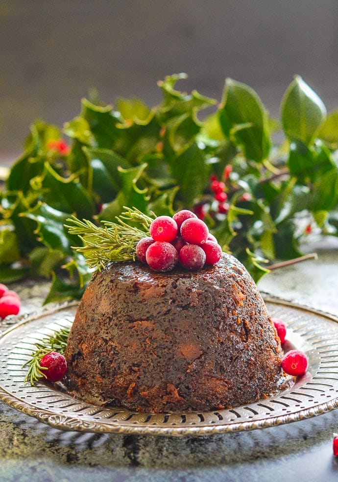 A side image of a Christmas pudding topped with fruit with holly in the background.