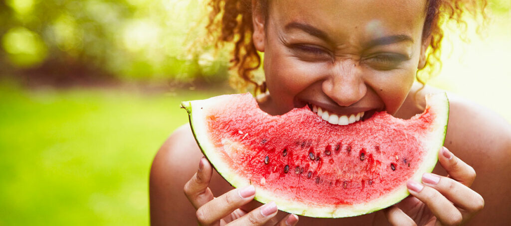 Woman eating from a wedge of watermelon, outside in the sun.