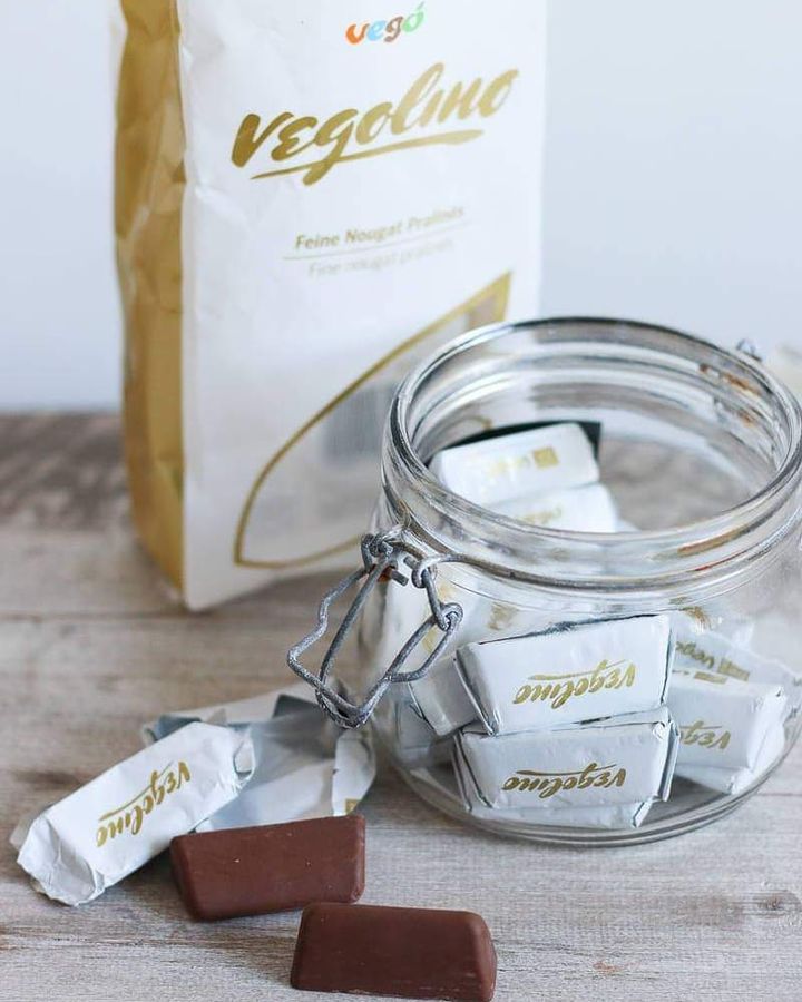 A bag of vegolino on a table behind a mason jar filled with wrapped chocolates. There are a few on display unwrapped in the foreground.