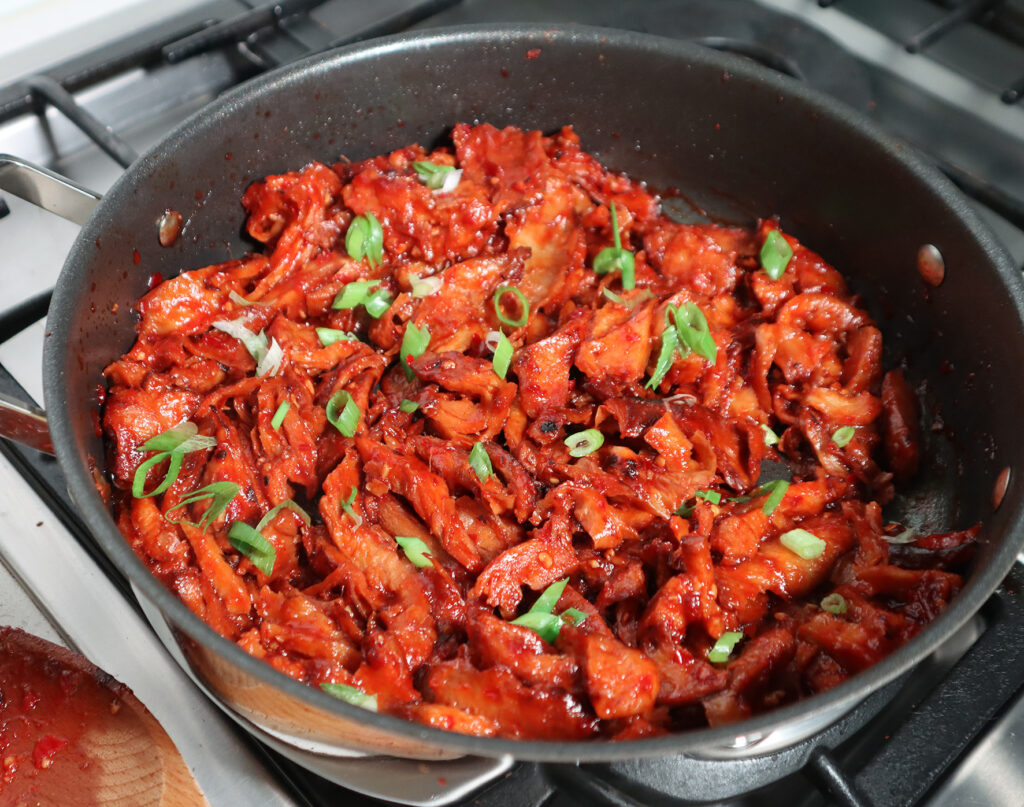 Marinated and bourbon-infused chicken shreds are in a pan on the stove.