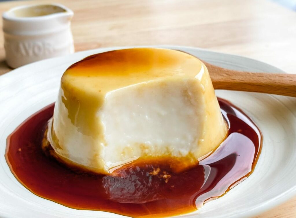 A side view of Purin, which looks like a creme caramel, with a bite taken out to show the smooth texture. 