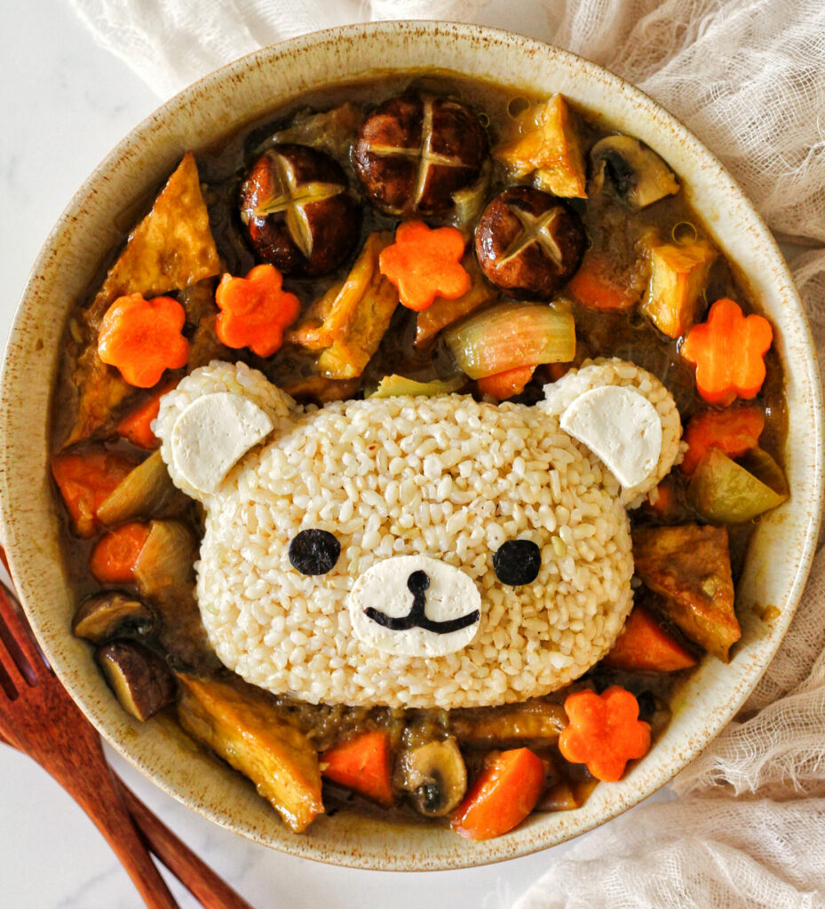 Overhead image of a bowl of curry. The veg are cut decoratively and the rice is served over top in the shape of a bear, with edible details.