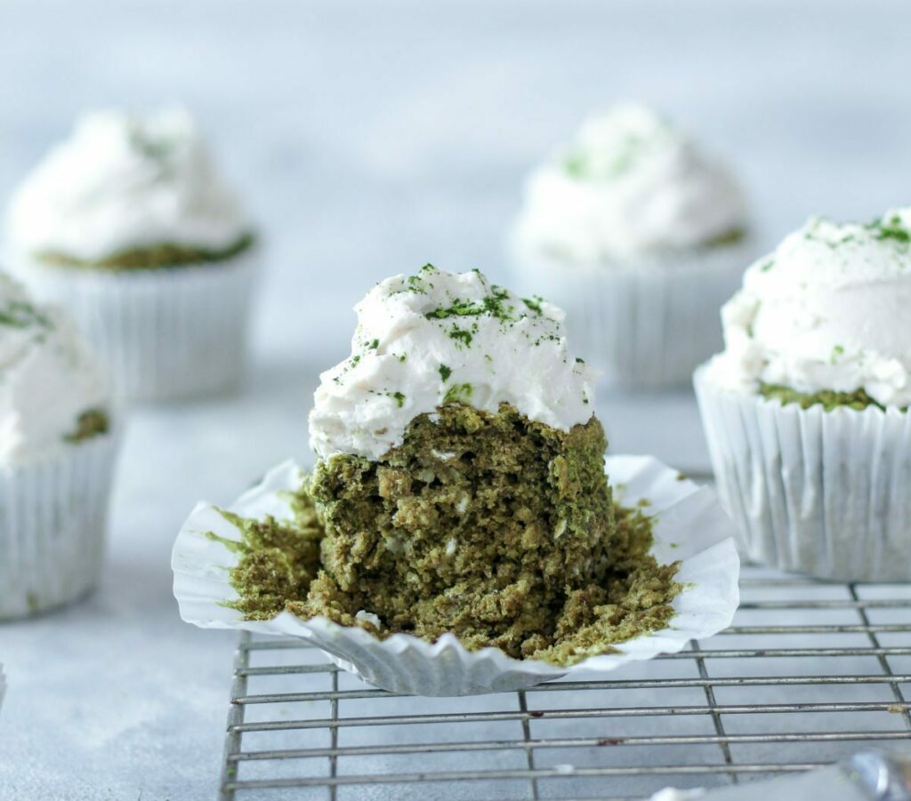 An image of a green tea matcha cupcake with white frosting with a chunk taken out, revealing a light and fluffy texture.