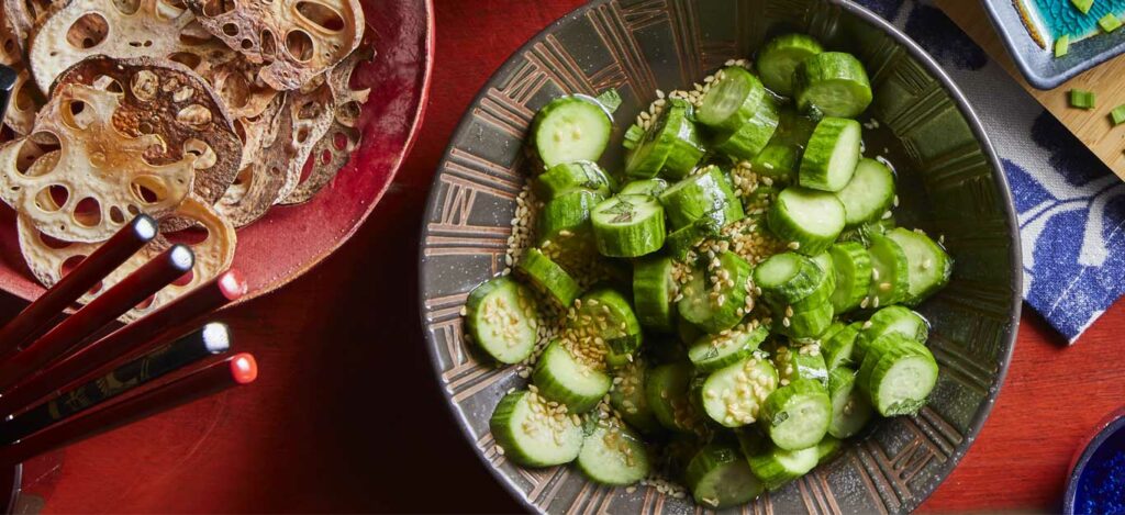 Overhead image of a bowl of pickled cucumbers topped with sesame seeds.