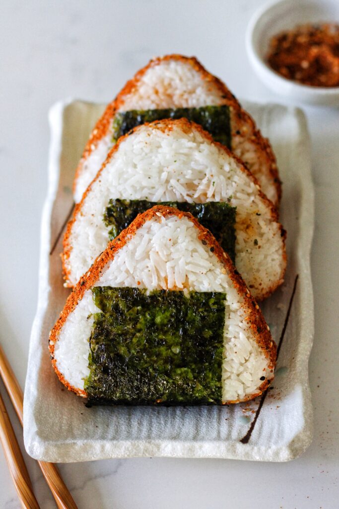 A frontal image of triangular onigiri with squares of seaweed on a rectangular serving platter.