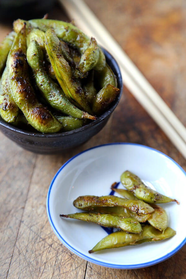 A serving bowl with edamame pods sits next to a small individual serve in a bowl.