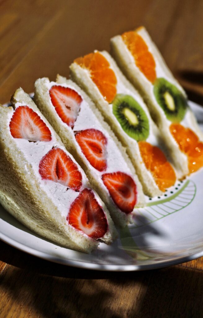 Two varieties of fruit sandwiches sit neatly on a plate outside. One has strawberry and cream, the other mandarin and kiwi fruit.