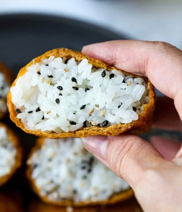 Inari being held up to camera showing fluffy rice in a thin deep-fried pocket.