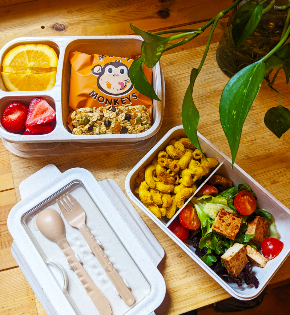 Overhead shot of an open lunchbox on a wooden bench, displaying a variety of plant-based and healthy treats.