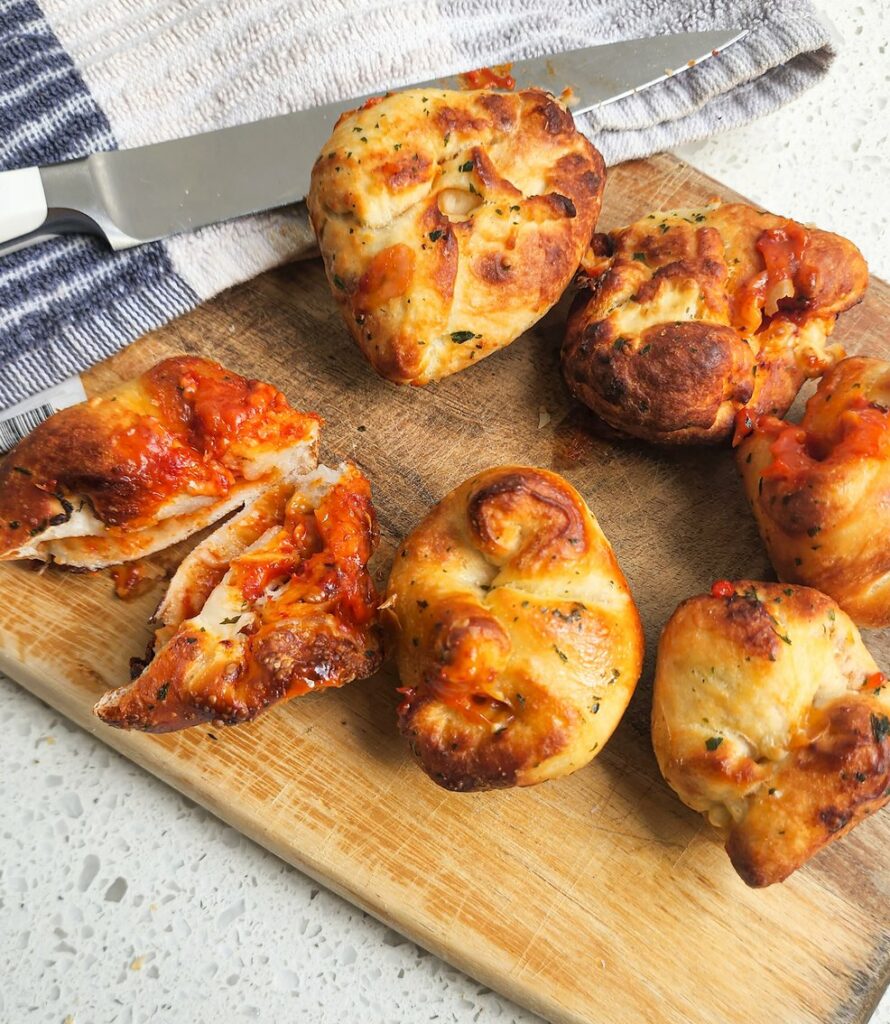 A shot of stuffed pizza dough balls on a wooden chopping board, one cut open to reveal cheese and tomato pizza fillings.