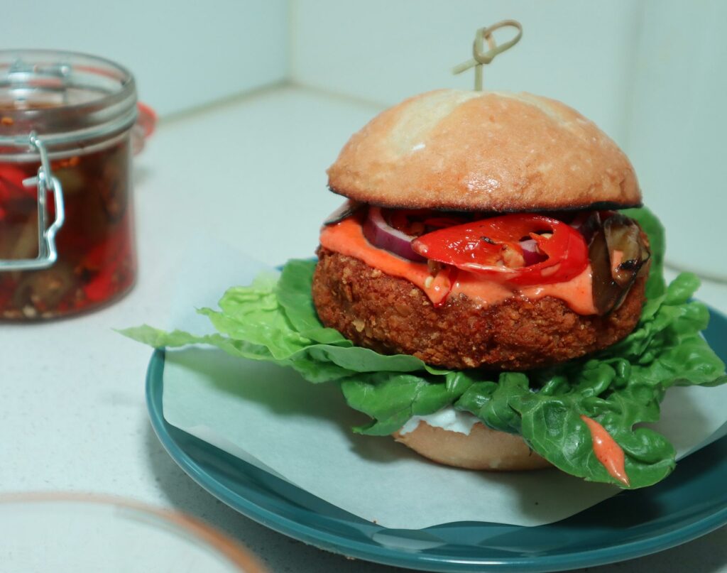 A burger sits on a plate with a chunky, perfectly crispy vegan 'chicken' patty, served with lettuce, tomato, onion and a zingy sauce.