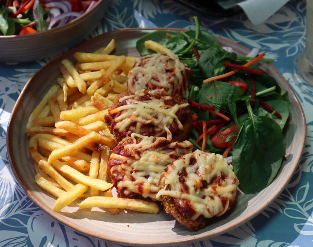 A plate full of mini vegan parmas served with chips and a green side salad.