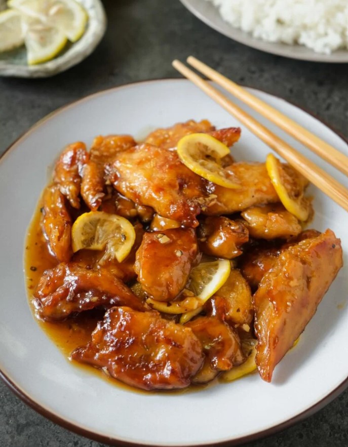 A bowl of lemon chicken pieces coated in a sticky, zesty marinade.