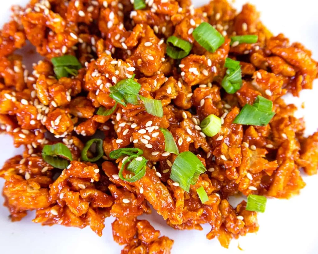 Close-up image of a plate of Korean-style fried 'chicken' garnished with spring onion and sesame seeds.