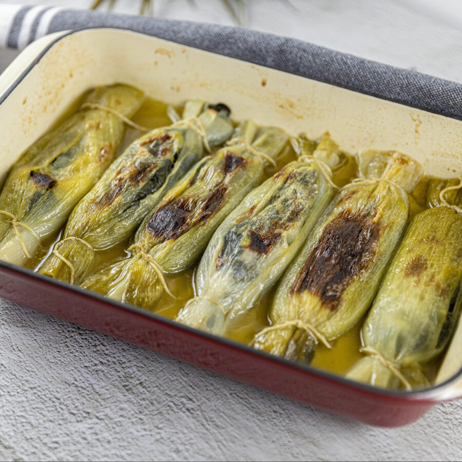 A rectangular oven tray filled with stuffed leeks in the shape of bonbons.