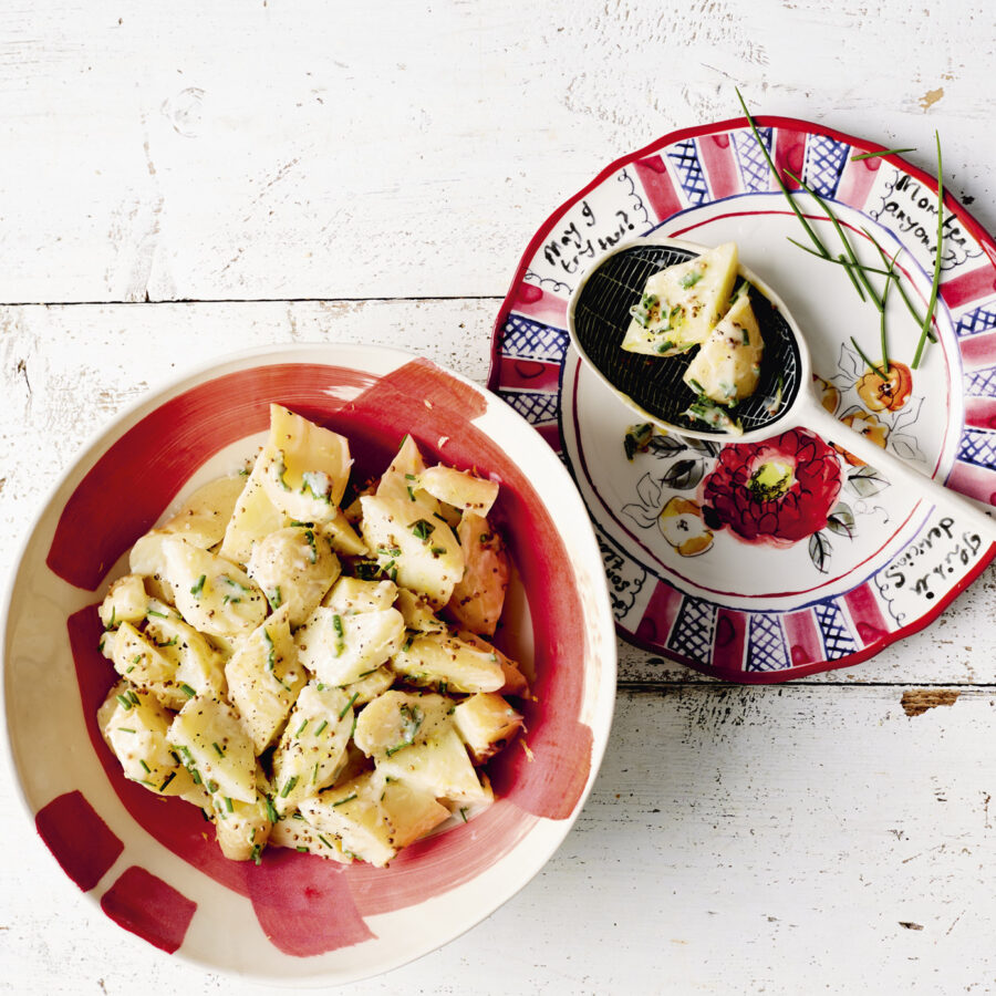 A bowl and plate of plant-based potato salad with chopped herbs on a white wooden surface, ideal for vegan lunch box inspiration.