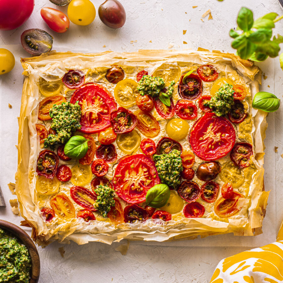A rectangular tart with flaky filo pastry topped with tomato and dollops of basil pesto.
