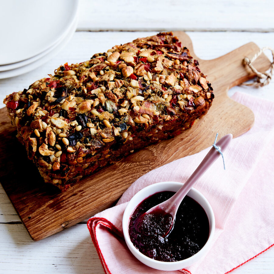 A rectangular nutloaf sits on a wooden serving board, with a side of cranberry sauce.
