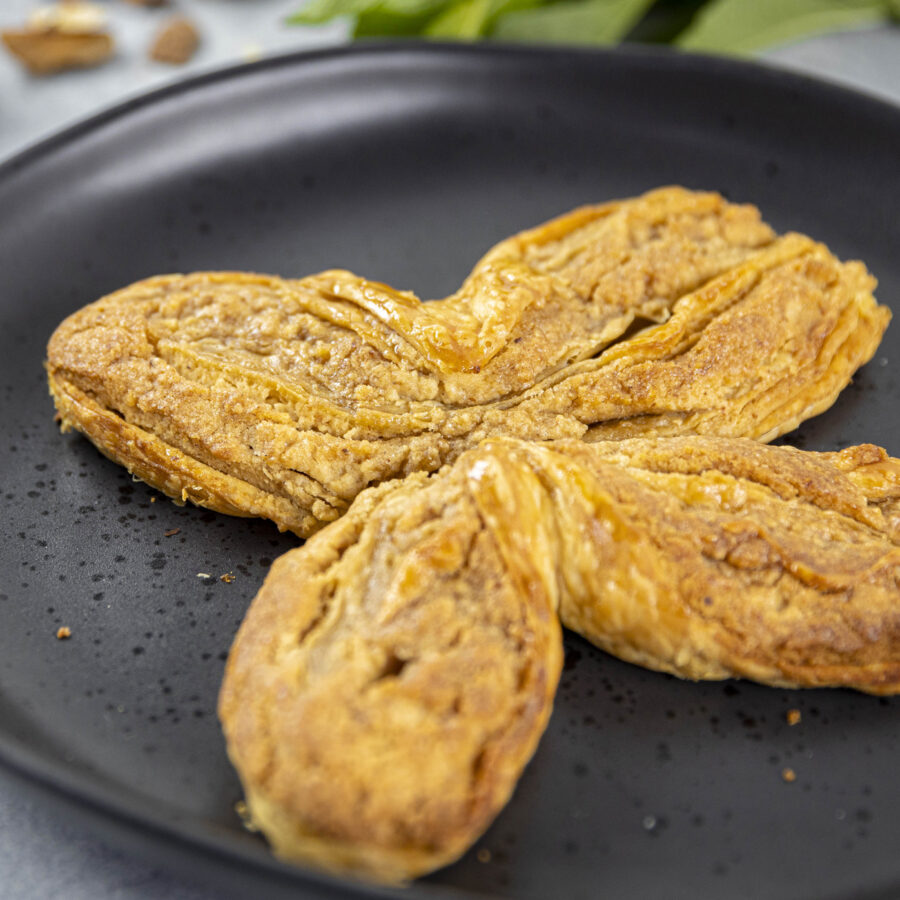 A four-leaf clover-shaped, plant-based pastry inspired by Armenian Gata is served on a black plate.